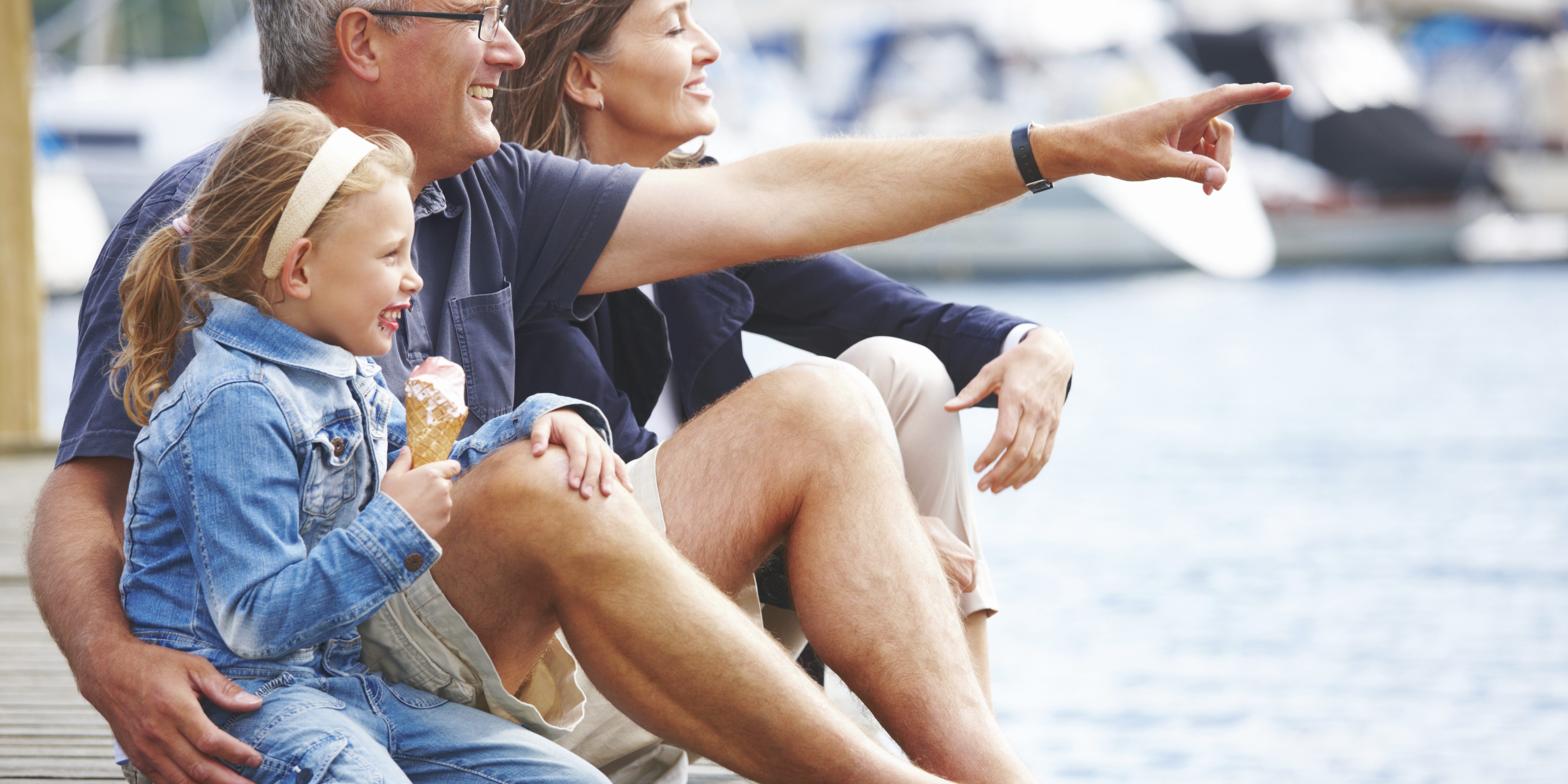 Happy Grandparents sitting with their granddaughter on a pier, pointing out at the boats - copyspace